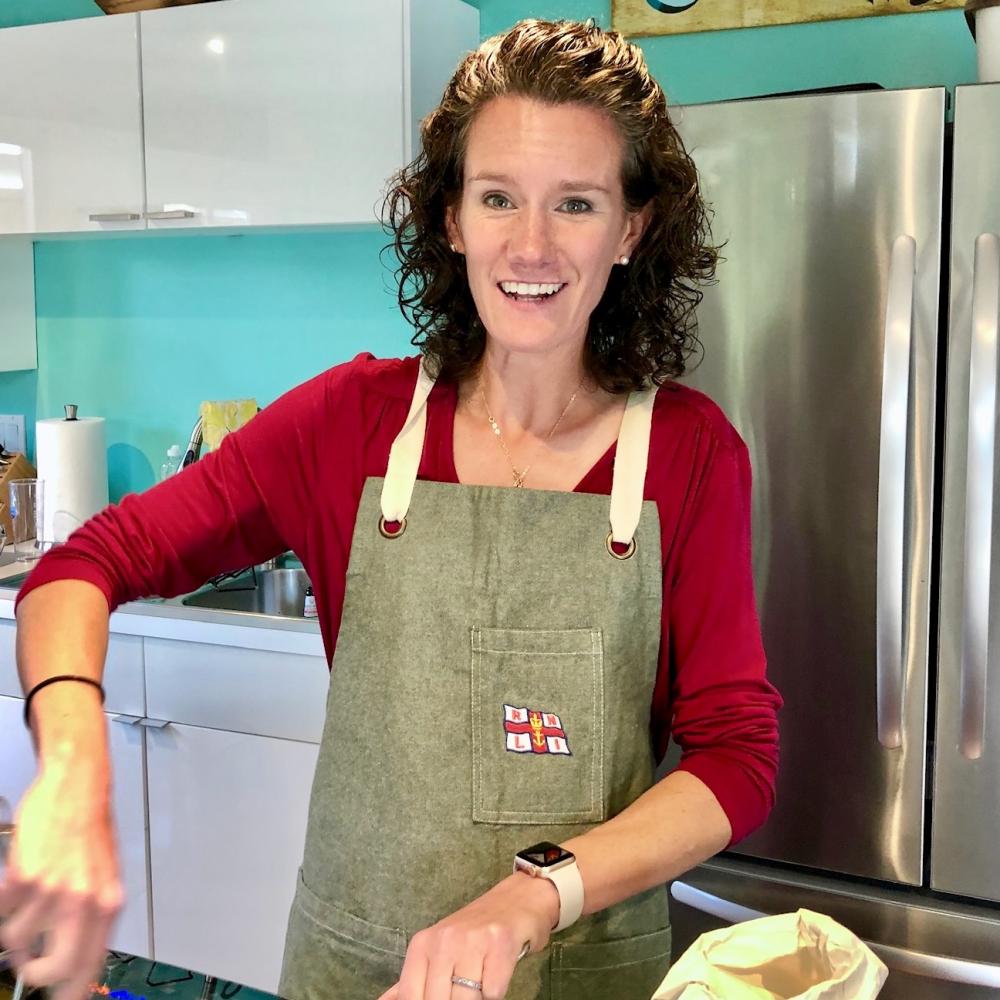 Smiling woman stirring a pan in a kitchen, wearing a green apron and red top
