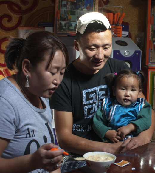 A family shares a meal together, with a man and woman helping a young child at a table.