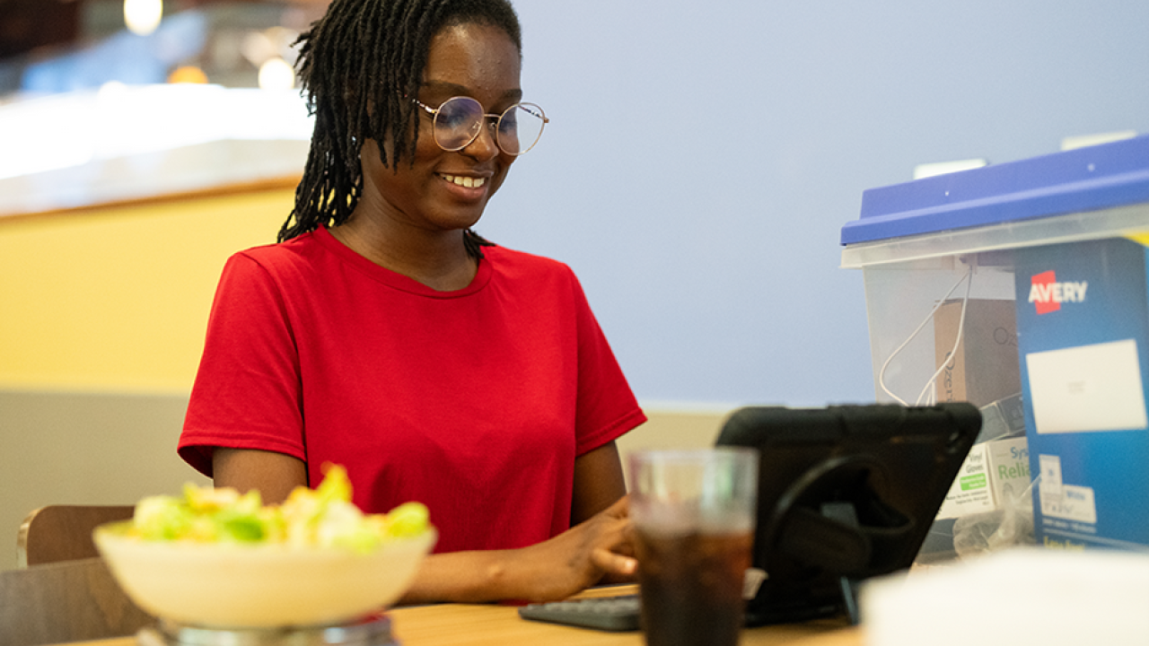 Christabel Domfe sitting at dining hall table at computer with FRANI App