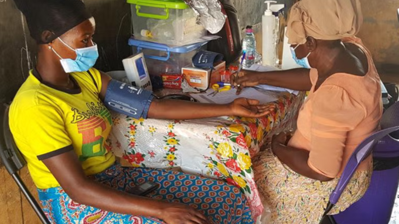 Nigerian woman patient being interviewed by Nigerian researcher at colorful table w/ research supplies