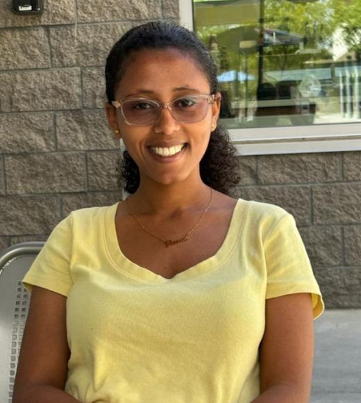 Lidya Abebe sitting outside in yellow shirt & glasses, smiling.