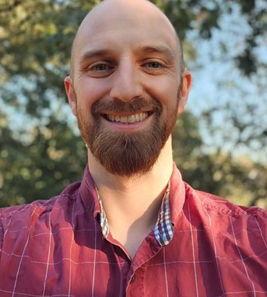Charles smiling selfie, red button down shirt, with brown lines, tree in background