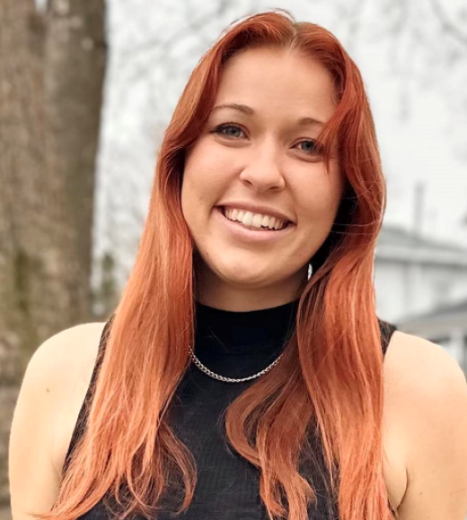 Madelyn smiling, in black sleeveless knit top; w/ long auburn hair