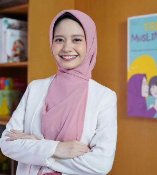 Davrina Rianda profile photo, smiling with pink head scrarf, white top, arm folded