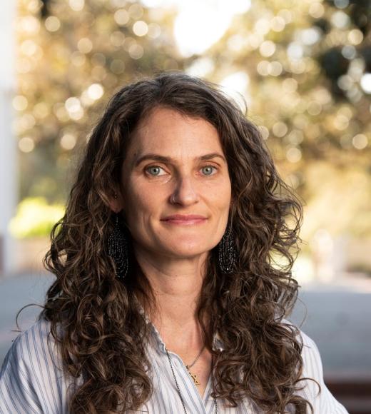 Leah looking at camera, long curly hair, white blouse w/small navy blue stripes