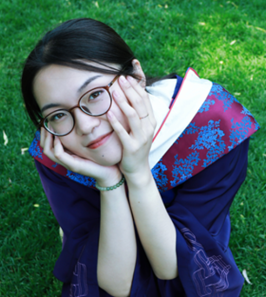 Shuangyu sitting with elblows on knees, face in her hands smiling, with red-purple kimono silk dress