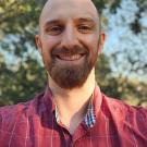 Charles smiling selfie, red button down shirt, with brown lines, tree in background