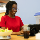 Christabel Domfe sitting at dining hall table at computer with FRANI App