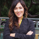 Jennifer Falbe, profile photo in black jacket with arms crossed, smiling