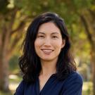 Katherine Kwon smiling, standing with arms folded on grass with trees in background