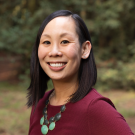 Lauren Au, profile photo, smiling face in burgundy dress, & big round jade stone necklaces
