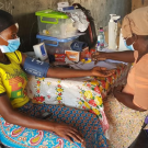 Nigerian woman patient being interviewed by Nigerian researcher at colorful table w/ research supplies