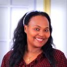 Debritu headshot, w/ hair in headband scarf & red-black checked shirt