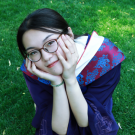 Shuangyu sitting with elblows on knees, face in her hands smiling, with red-purple kimono silk dress